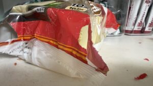 さいたま市の住宅のキッチンで、ネズミに食い破られた赤い食品パッケージ。周囲に袋の破片が散乱しています。